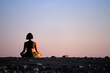 © Cavan Images - Woman meditating on the beach at sunset.