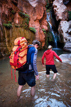 A Man And Woman Wade Through Water In A Canyon.