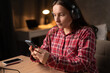 © Andrii Lysenko - Woman listening to music using headphones and mobile phone sitting at table in the dormitory or at home at night.