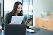 © Jirapong - Portrait of a young Asian woman showing a smiling face as she uses his phone, computer and financial documents on her desk in the early morning hours