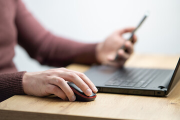 Close up of a man working on laptop and using smartphone. Businessman using smartphone while working on laptop in the office on a desk