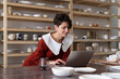 © DimaBerlin - Smiling successful craftswoman ceramic artist using craft platform to sell pottery items, female artisan working on laptop while standing against wooden bookcase with handcrafted ceramics in workshop
