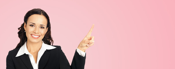 Sticker - Young happy smiling woman in black confident suit, showing pointing at copy space. Business concept. Rose pink color background. Brunette businesswoman. Wide.