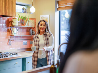 Poster - Smiling woman carrying tea for friend in kitchen