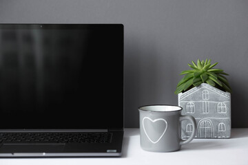 Freelance. The office is designed in light gray tones. A white table with a laptop, a flower and a mug. Work at home. The beginning of the working day. Office interior concept.