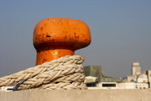 Bright Orange Mooring Pole For Mooring Ships With A Rope Wrapped Around It In A Seaport
