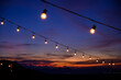 Festoon string lights decoration at the party event festival against sunset sky. light bulbs on string wire with copy space. Outdoor holiday background.