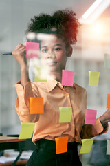 Wall Mural - Young smiley attractive businesswoman using sticky notes in glass wall to writing strategy business plan to development grow to success