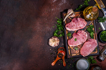 Wall Mural - Raw pork steaks cooking background. Three tasty raw fresh meat steaks with herbs, salt, pepper, olive oil, ready for dinner preparation, dark brown kitchen background copy space