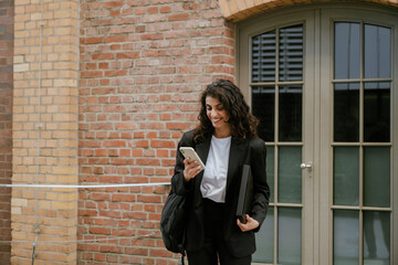 Wall Mural - Young brunette businesswoman using cellphone while walking outdoors