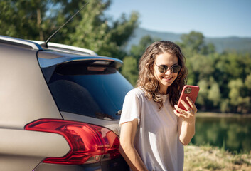 Wall Mural - Happy young woman driver traveler in sunglasses using smartphone during summe adventure travel