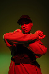 Wall Mural - african american woman in sweatshirt and baseball cap posing with crossed arms on green with red light.