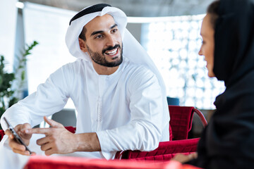 Wall Mural - Man and woman with traditional clothes working in a business office of Dubai. Portraits of  successful entrepreneurs businessman and businesswoman in formal emirates outfits.