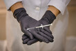© Talita - Sao Paulo, SP, Brazil - January 22 2023: Person in white coat and black gloves holding syringe with needle details.
