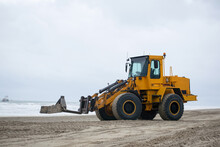 Yellow Bulldozer Excavating Sand On Dutch Beach Working. Clouded Weather Seashore Netherlands. Heavy Work Equipment. 