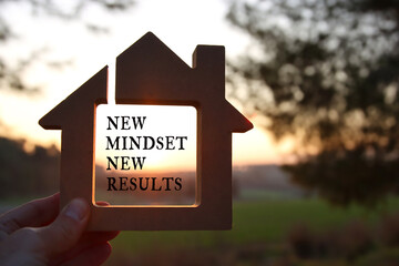 Poster - Hand holding wooden house with the text new mindset in front of the sunset
