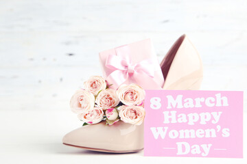 Wall Mural - Bouquet of roses, gift box and card with text 8 March Happy Womens Day, and beige high-heeled shoe on white wooden background