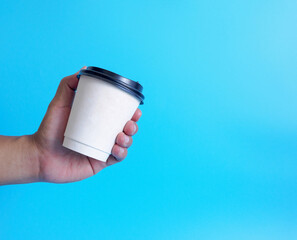 Wall Mural - Closeup young adult man hand holding white cup paper of coffee hot drink ready to drink refreshing. aroma awake fresh to work placed on a blue isolated background. Point of view shot.