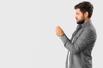 Wall Mural - Handsome young businessman using tablet computer on light background