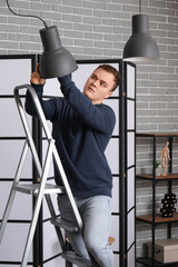 Young man on ladder changing light bulb in room