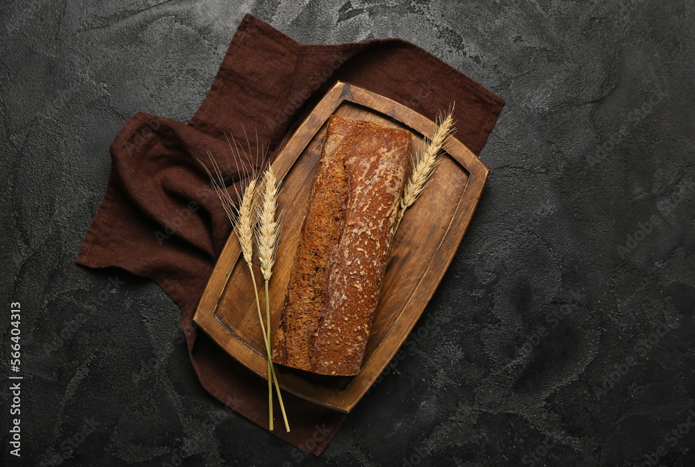 Board with loaf of fresh rye bread and wheat ears on black background