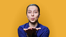 Teenage Female Making Air Kiss Looking At Camera On Yellow Background