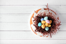 Easter Bundt Cake With Chocolate Nest Of Colorful Candy Eggs. Above View On A White Wood Background.