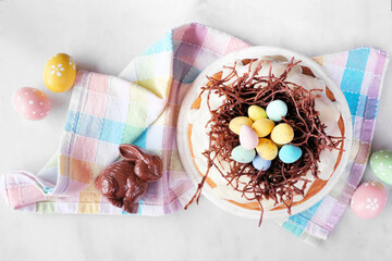 Poster - Easter bundt cake with chocolate nest of colorful candy eggs. Top view table scene over a white stone background.