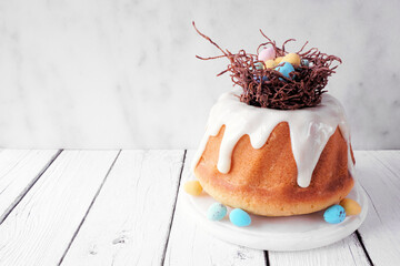 Poster - Easter bundt cake with chocolate nest of colorful candy eggs. Side view against a bright wood background.