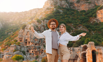 Sticker - Happy tourist couple man and woman archaeologist in hat background old tomb Myra Ancient City in Demre to Antalya. Concept travel of Turkey