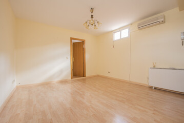 Wall Mural - Empty living room with light yellow walls, light wooden floor, electric heater, oak wooden door, split air conditioner, skylights high on the walls and ceiling lamp with white shade