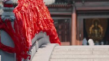 Red Silky Prayer Ribbon On White Stone Bridge Swaying In Wind With Buddha Status Background In Temple, 4k Slow Motion Footage.