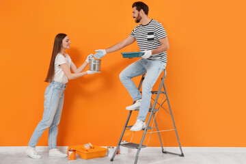 Canvas Print - Woman giving can of paint to man near orange wall indoors. Interior design