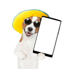 Poster - Happy Jack russell terrier wearing sunglasses and summer hat holds big smartphone with white blank screen in it paw, showing close to camera. isolated on white background