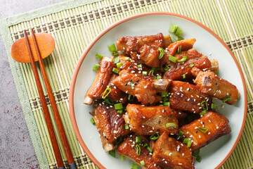 Chinese sweet and sour ribs with green onion and sesame close-up in a plate on the table. Horizontal top view from above