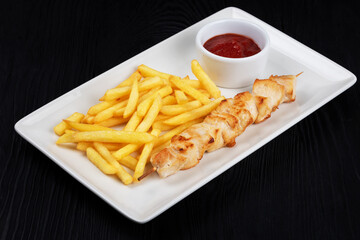 Wall Mural - Grilled chicken shashlik meat with fried potatoes on white plate on black wooden background