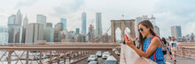 New York Woman Using Phone App Walking On Brooklyn Bridge By Manhattan City Skyline. Young Female Professional Multicultural Lady, New York City, USA. Panoramic Banner