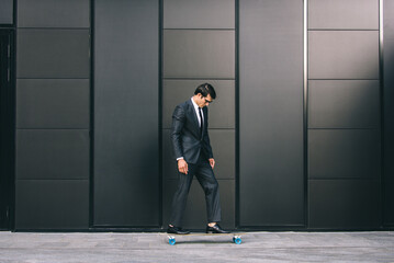 Wall Mural - Young handsome man with business suit riding on a longboard - Corporate businessman portrait, concepts about business, mobility and lifestyle