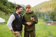 © Drobot Dean - Two white man smiling and using cellphone while walking in forest