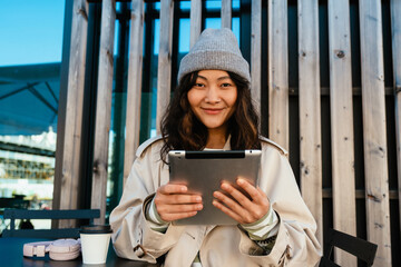 Wall Mural - Young asian woman smiling and using tablet computer in cafe outdoors