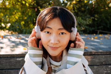 Wall Mural - Young asian woman listening to music with headphones outdoors