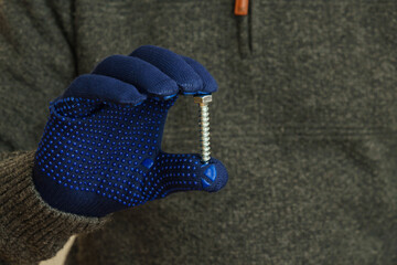 Man hand in blue gloves holding a large metal bolt. Close up.