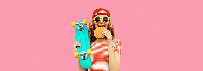 Wall Mural - Portrait of stylish young woman with burger fast food and skateboard wearing baseball cap, sunglasses on pink background