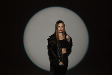 Wall Mural - Stylish beautiful glamorous girl in fashion black rock casual clothes with top and leather jacket on a dark background with circular light at a party in the studio