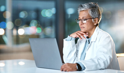 Laptop, doctor and senior woman in hospital working late or overtime on email, telehealth or research. Bokeh, thinking and female medical physician reading healthcare information at night on computer