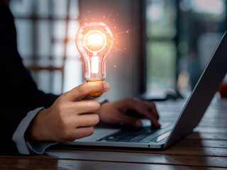 Poster - Searching online concept. magnifying glass icon in creative idea light bulb holding by business person hand who working with laptop computer. Digital search technology, learning and education.