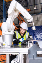 young female asian service engineer holding robot controller operate robot arm automation factory