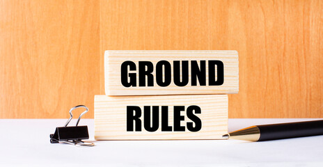 A pen, a paper clip and two wooden blocks with the text GROUND RULES on a light wooden background