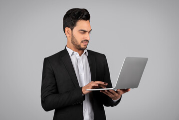 Young Middle Eastern Businessman In Suit Using Laptop Computer Over Grey Background