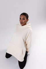 Wall Mural - Attractive african american woman in oversized white hoodie sits on white background.